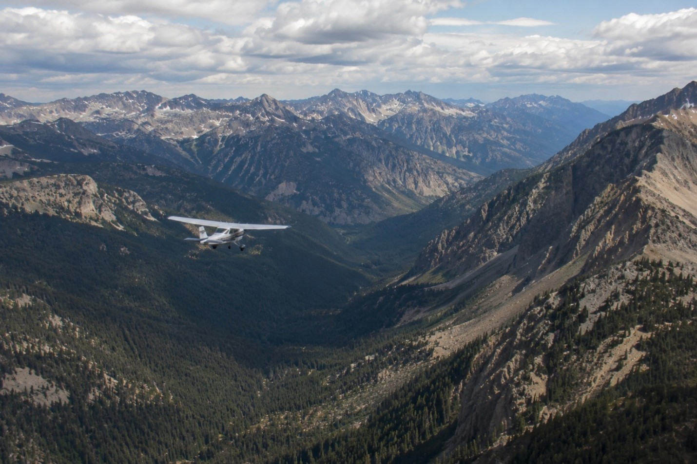 A light airplane flying through a mountain valley surrounded by rugged peaks.