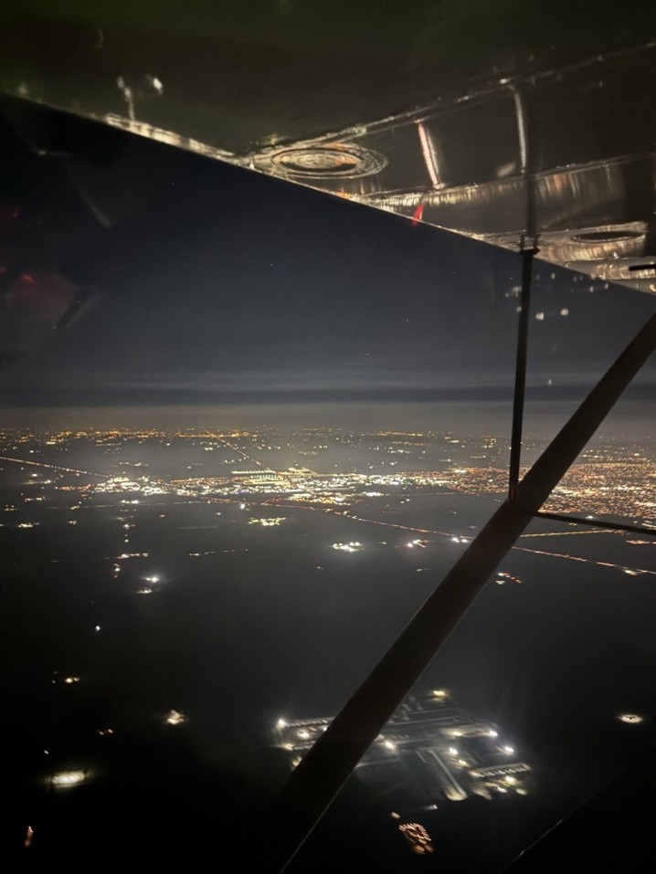 City lights at night seen beneath the wing and strut of a light airplane.